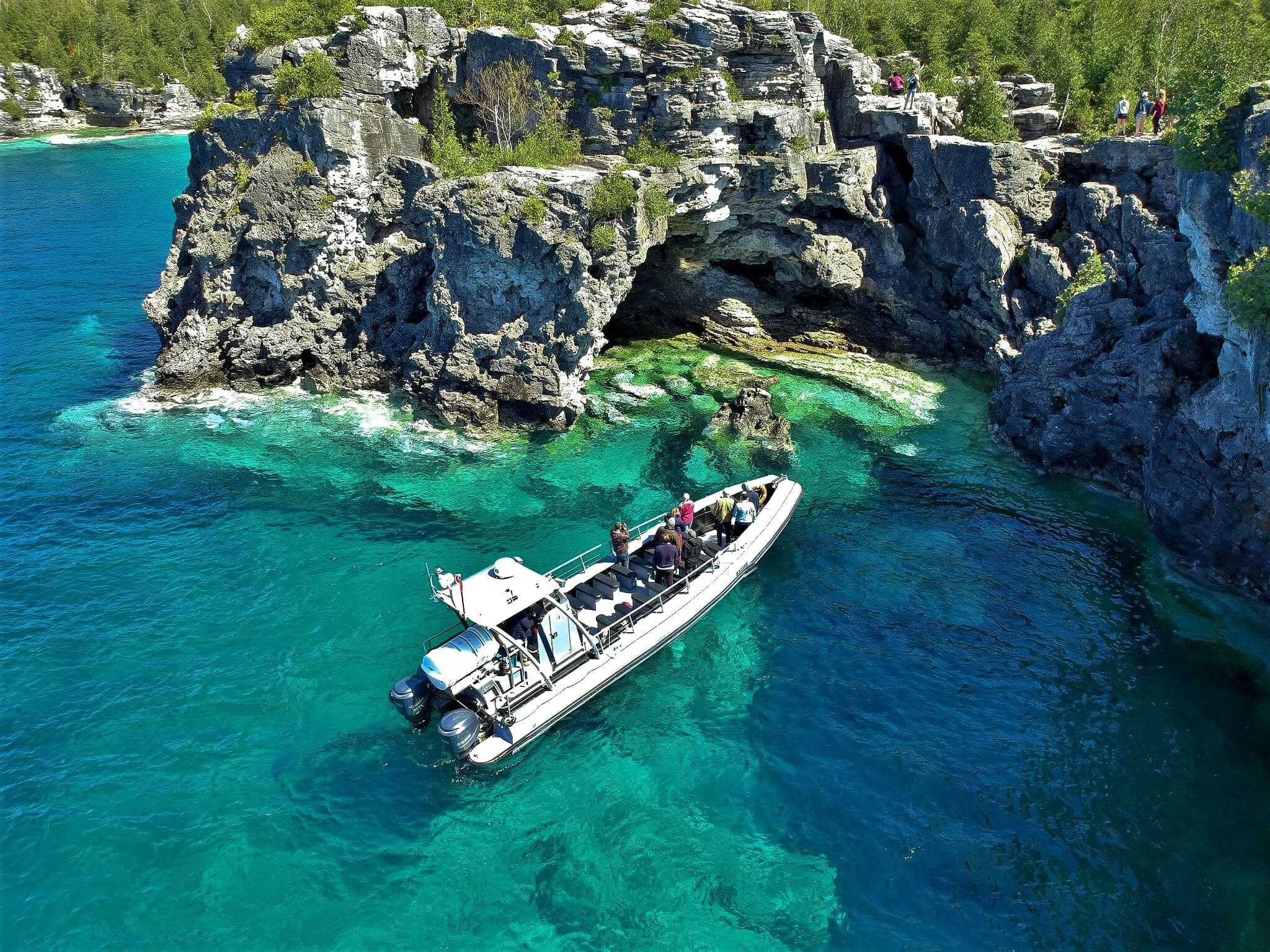 Open air tour boat close to a sea cave in clear blue water.